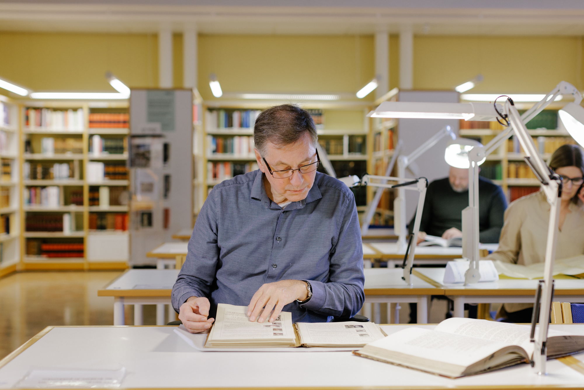 Mann som sitter på lesesal og blar i en gammel bok