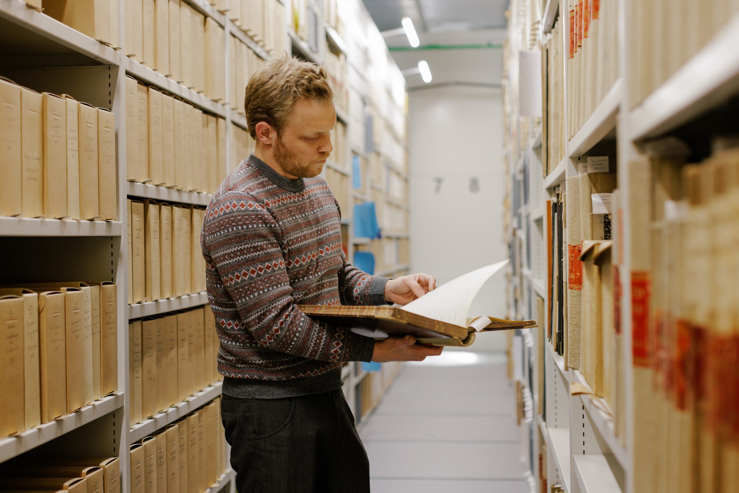 Mann står mellom to arkivreoler og blar i en gammel arkivprotokoll 