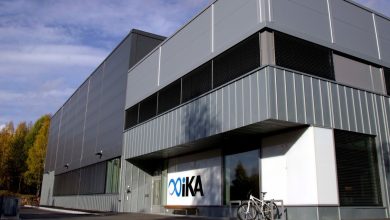 Stort grått og hvitt bygg i 3 etasjer. Logo - IKA Kongsberg. Skog i bakgrunnen.