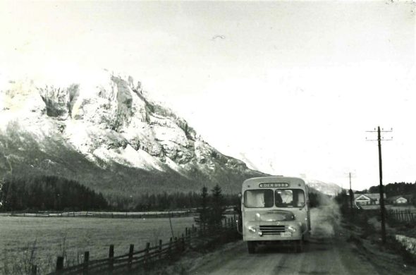 Bokbuss som kjører på vei i Hemsedal med snødekte fjell i bakgrunnen 1953