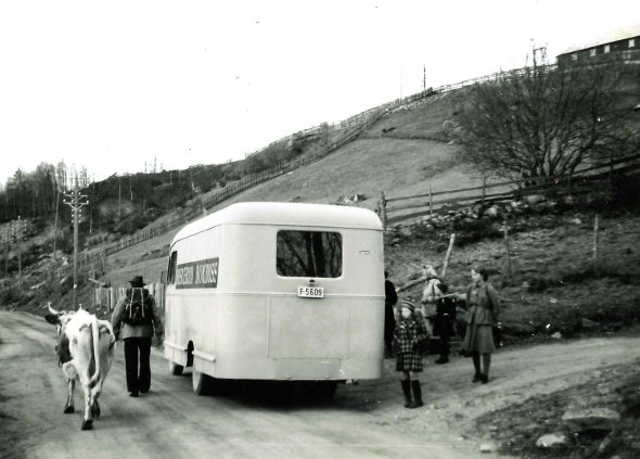 Bokbuss som har stoppet langs veien i Kvisla, mann med ku i forgrunn, kvinne og barn venter ved bussen 1951