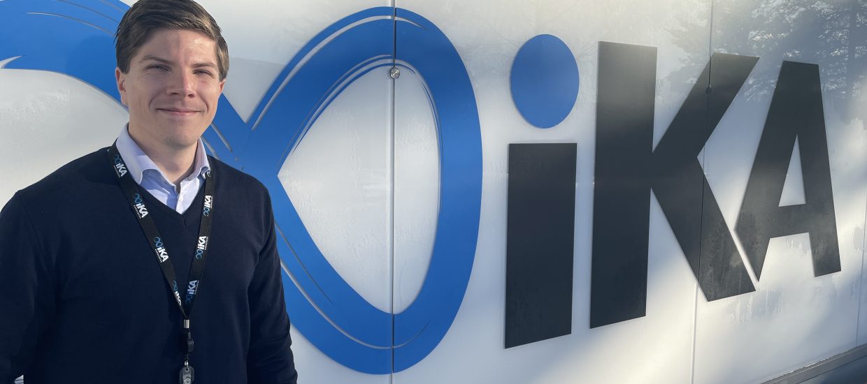 Mann i blå genser står foran en vegg med logoen til IKA Kongsberg.